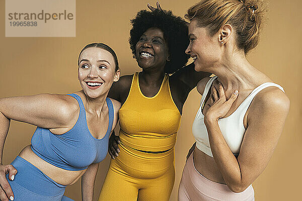 Cheerful multiracial female friends against beige background