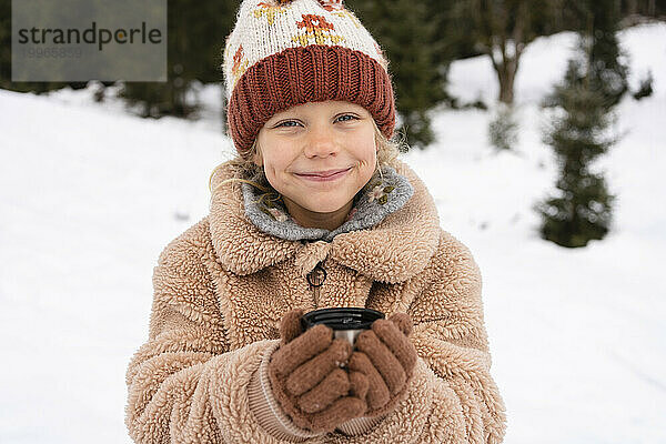 Lächelndes Mädchen hält Tee im Winterwald