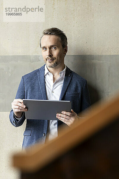 Reifer Geschäftsmann mit Tablet-PC vor der Wand