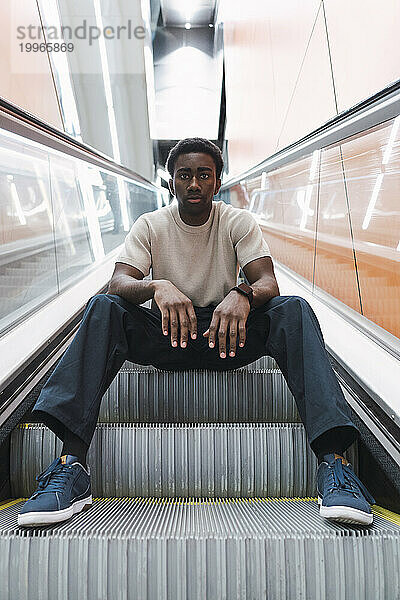 Junger Mann sitzt auf der Rolltreppe einer U-Bahn-Station