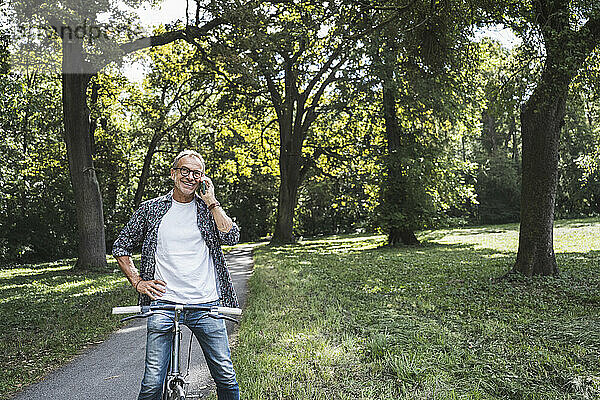 Älterer Mann mit Fahrrad telefoniert im Park