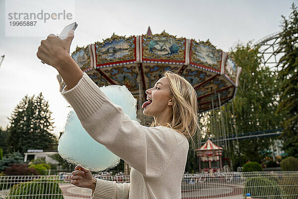Glückliche Frau leckt Zuckerwatte und macht ein Selfie im Vergnügungspark