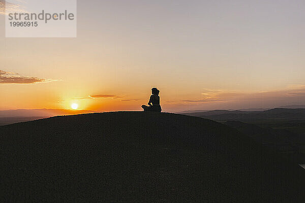 Frau sitzt und schaut auf den Sonnenuntergang