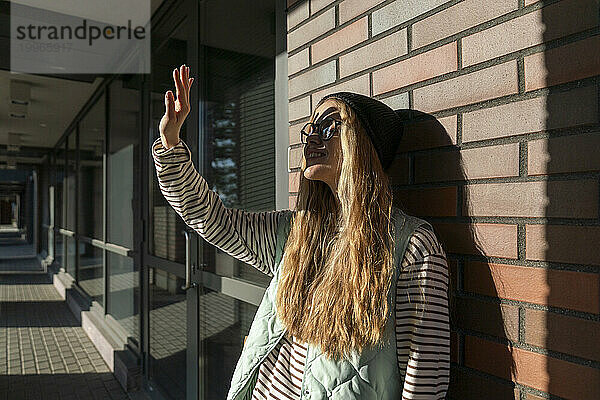 Blonde Frau schützt ihre Augen vor Sonnenlicht vor einer Ziegelwand