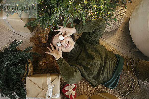 Playful woman holding Christmas ornaments on eyes at home
