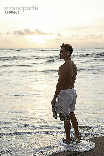 Shirtless man standing in sea water at beach