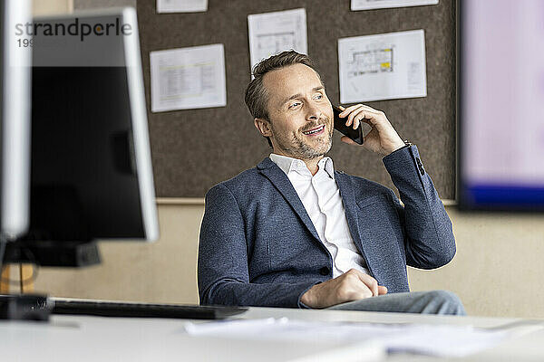 Reifer Geschäftsmann  der im Büro auf dem Smartphone spricht