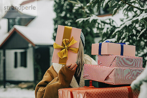 Frau hält Weihnachtsgeschenk über Gesicht neben Baum