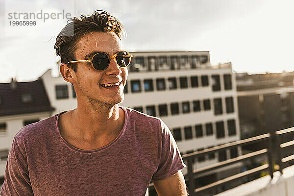 Smiling man wearing sunglasses on rooftop at sunset