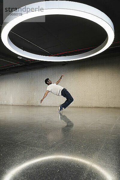Young man with futuristic cyber glasses break dancing under modern ring lamp