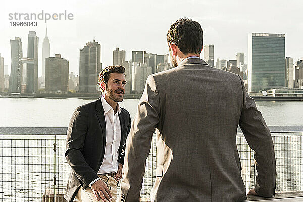 Lächelnder Geschäftsmann im Gespräch mit einem Kollegen am Hudson River in New York City  USA