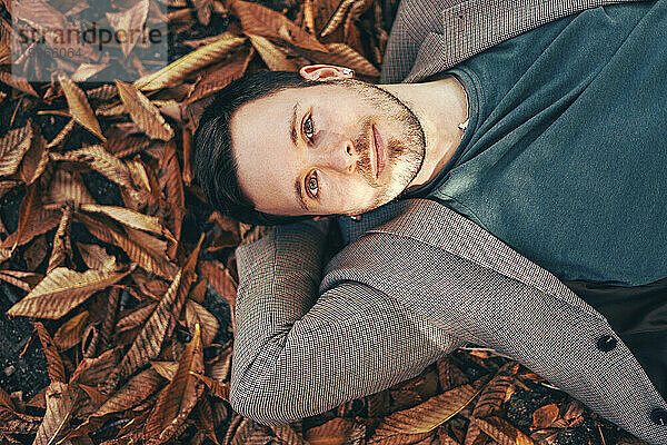Lächelnder junger Mann  der sich auf Herbstblättern entspannt