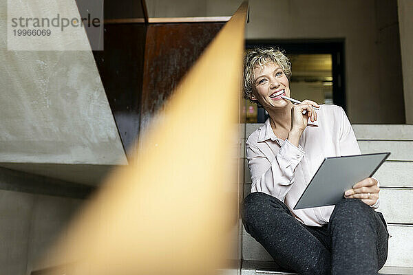Glückliche Geschäftsfrau mit Tablet-PC sitzt auf der Treppe