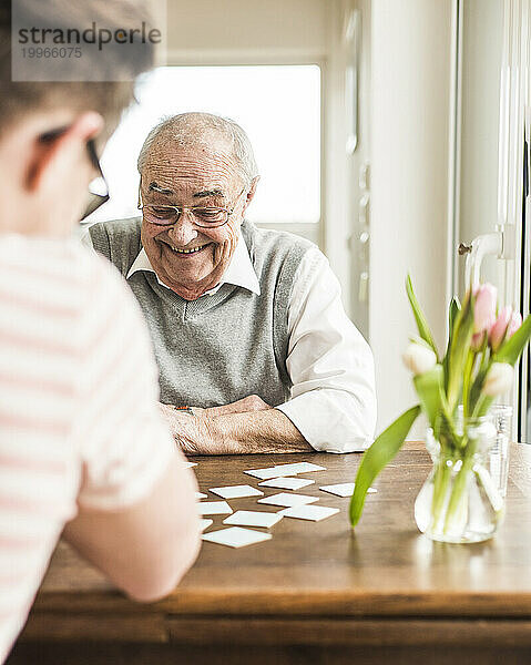 Happy grandfather playing cards with grandson at home