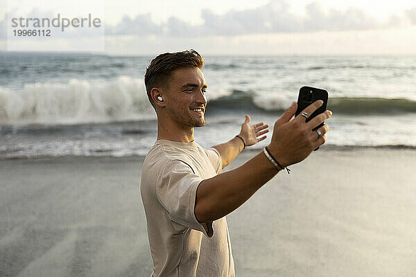 Glücklicher Mann zeigt das Meer per Videoanruf per Smartphone am Strand