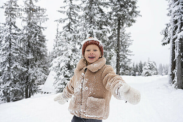 Fröhliches Mädchen mit ausgestreckten Armen genießt den Winterwald