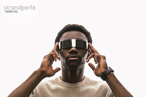 Cooler junger Mann mit Cyberbrille vor weißem Hintergrund  der die Finger auf die Schläfen legt