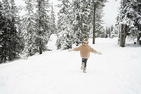 Mädchen läuft in der Nähe von Bäumen im Winterwald