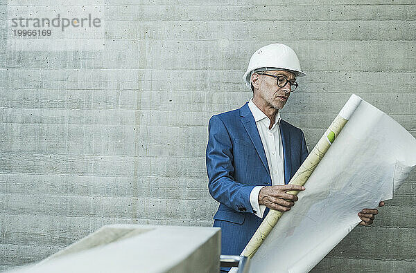 Ingenieur trägt Schutzhelm und untersucht den Bauplan in der Nähe der Wand