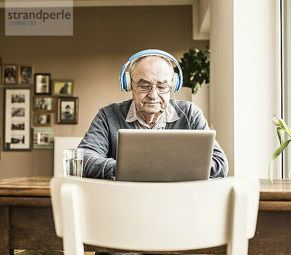 Älterer Mann trägt Kopfhörer und benutzt Laptop zu Hause