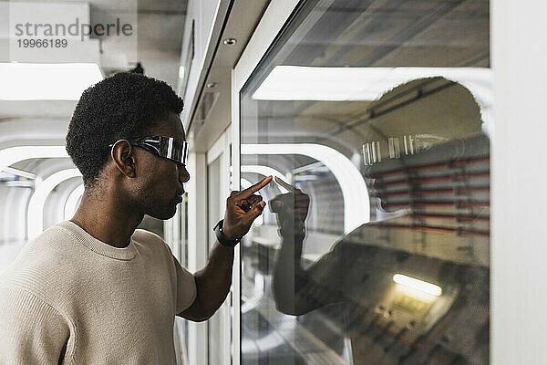 Young man with cyber glasses touching glass pane with his forefinger