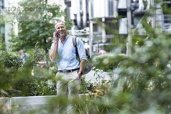 Glücklicher Geschäftsmann  der im Büropark mit dem Smartphone spricht