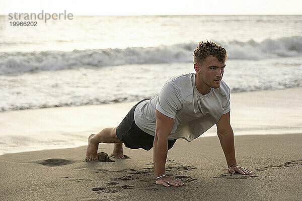 Junger Mann macht Liegestütze im Sand am Strand