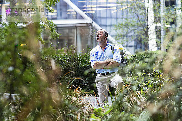 Geschäftsmann mit verschränkten Armen steht im Büropark