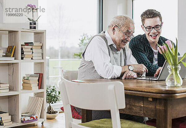 Happy young man teaching laptop to grandfather at home