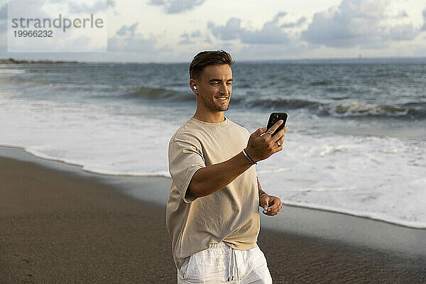 Lächelnder Mann  der am Strand per Videoanruf über sein Smartphone spricht