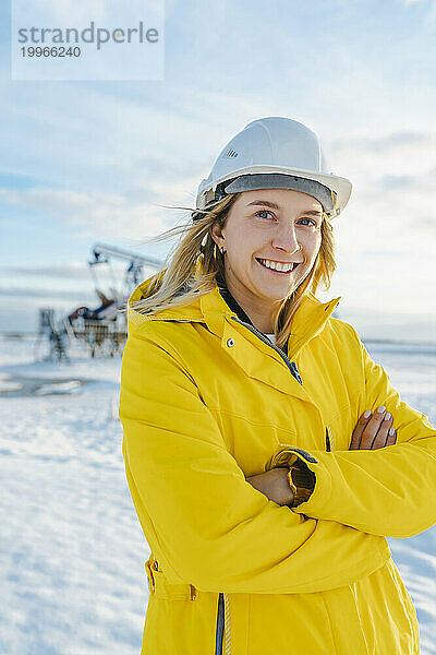 Lächelnder Ingenieur mit verschränkten Armen am Ölförderfeld im Winter