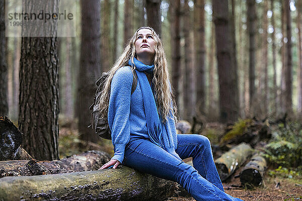 Nachdenkliche schöne Frau sitzt auf einem Baumstamm im Cannock Chase Forest