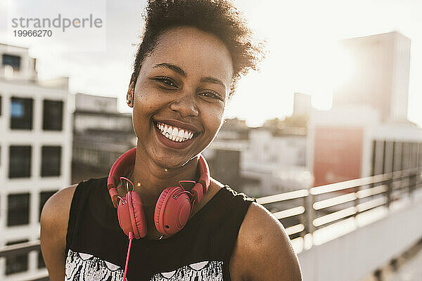 Lächelnde junge Frau mit Kopfhörern auf dem Dach