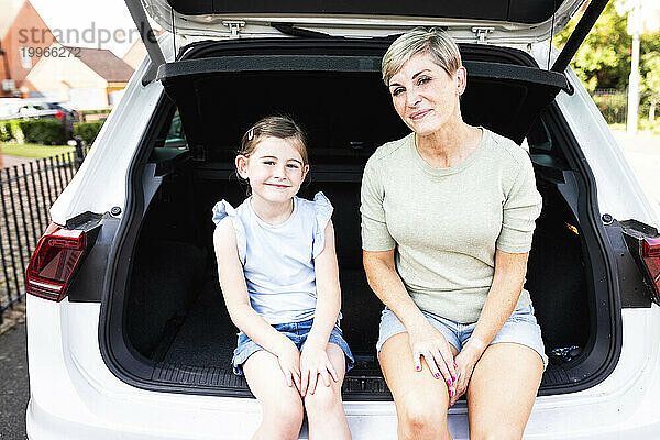 Lächelnde Mutter und Tochter sitzen zusammen im Kofferraum eines Autos
