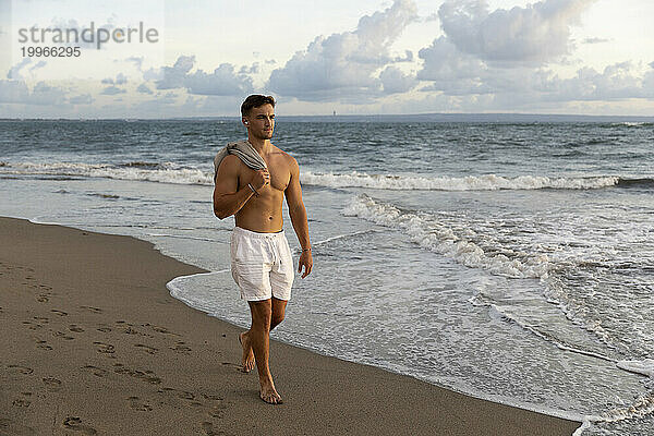 Mann ohne Hemd geht am Strand am Meer entlang