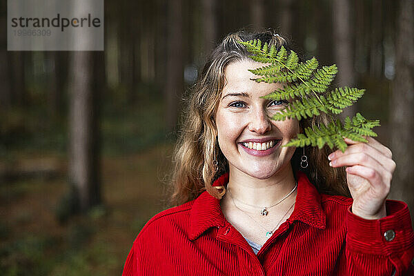 Lächelnde schöne Frau hält Farnblatt im Wald von Cannock Chase