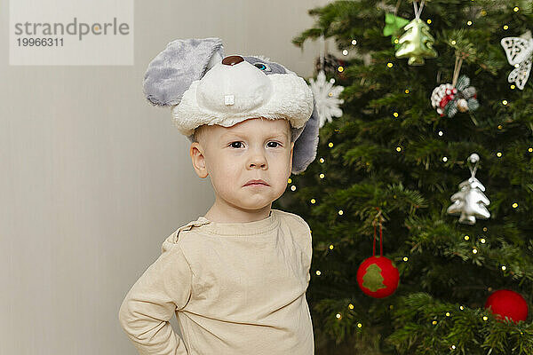 Trauriger Junge steht zu Hause neben dem Weihnachtsbaum vor der Wand