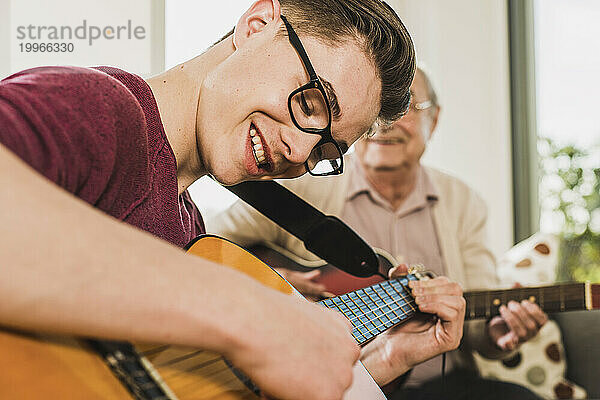 Glücklicher junger Mann  der zu Hause mit seinem Großvater Gitarre spielt