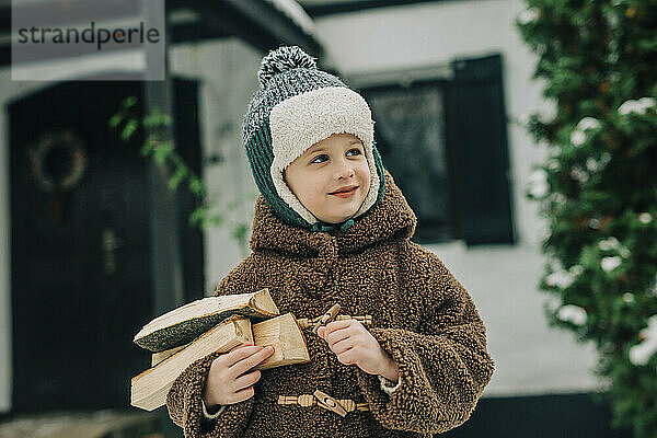 Lächelnder Junge trägt warme Kleidung und trägt Brennholz