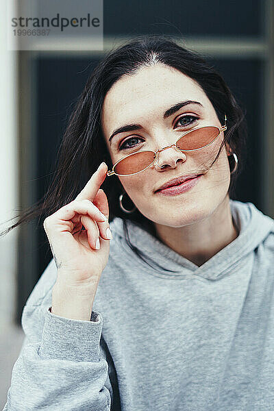 Lächelnde Frau  die Retro-Sonnenbrille berührt