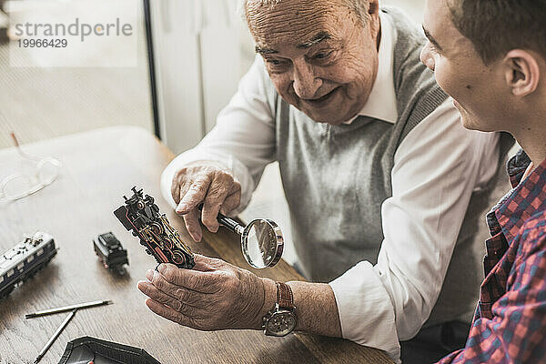 Glücklicher älterer Mann zeigt seinem Enkel zu Hause eine Miniatur-Spielzeugeisenbahn