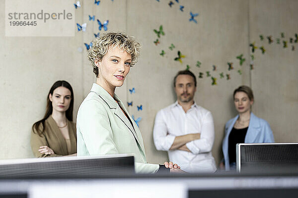 Selbstbewusste Geschäftsfrau mit Kollegen im Hintergrund im Büro