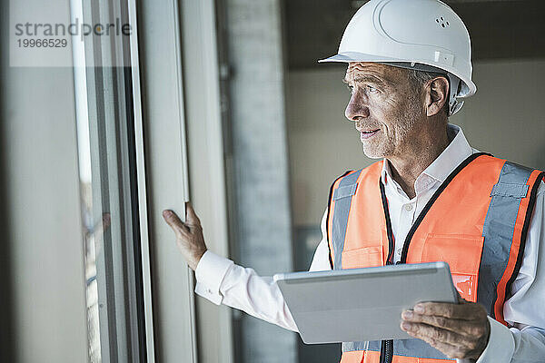 Ingenieur hält Tablet-PC in der Hand und schaut durch das Fenster