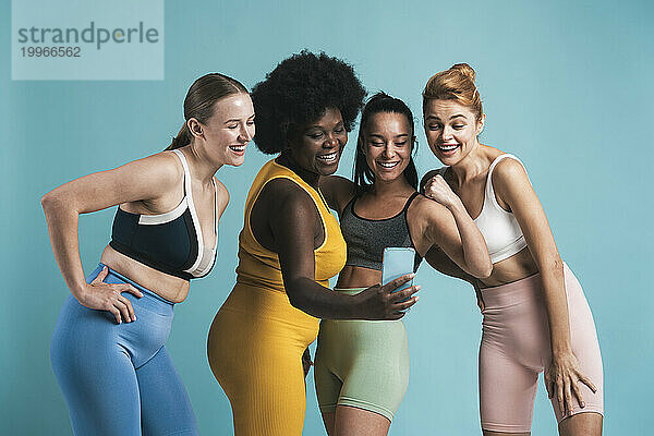 Glückliche Frau  die ein Selfie mit Freundinnen macht  die vor blauem Hintergrund lachen