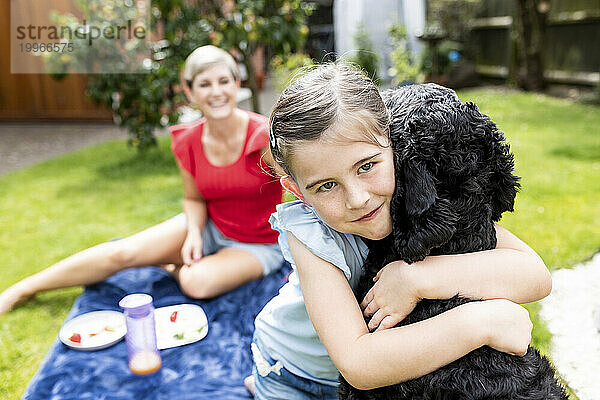 Lächelndes Mädchen umarmt Hund im Garten