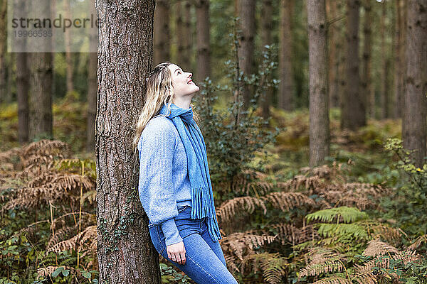 Glückliche Frau lehnt an Baum im Cannock Chase Forest