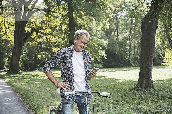 Älterer Mann mit Fahrrad und Smartphone im Park