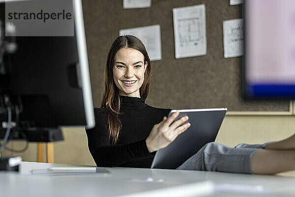 Glücklicher junger Auszubildender mit Tablet-PC am Arbeitsplatz