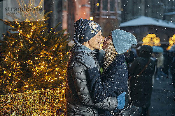 Liebespaar umarmt und reibt sich die Nase neben dem beleuchteten Weihnachtsbaum