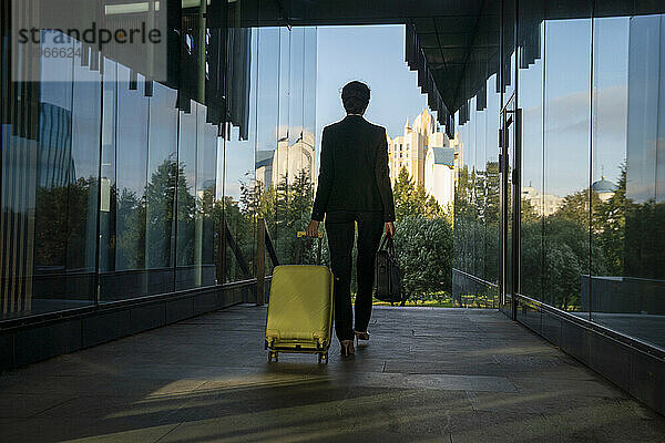 Geschäftsfrau zieht Koffer inmitten einer Glaswand